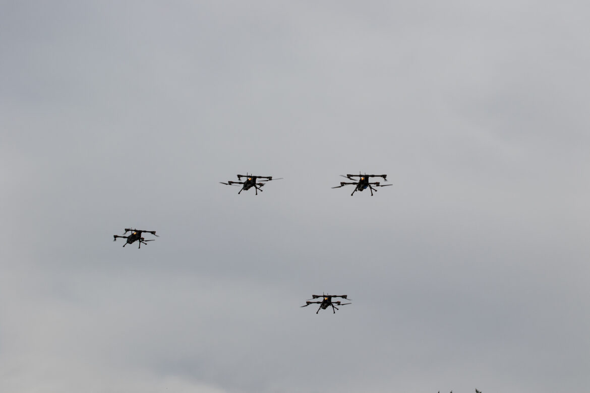 Čtyři experimentální drony T-Swarm 800 za letu proti šedé obloze.