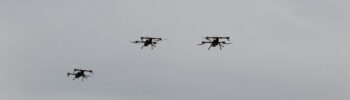 Čtyři experimentální drony T-Swarm 800 za letu proti šedé obloze.