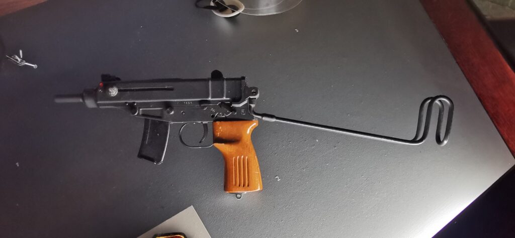 korpion vzor 61 s vyklopenou drátěnou ramenní opěrkou v muzejní vitríně.