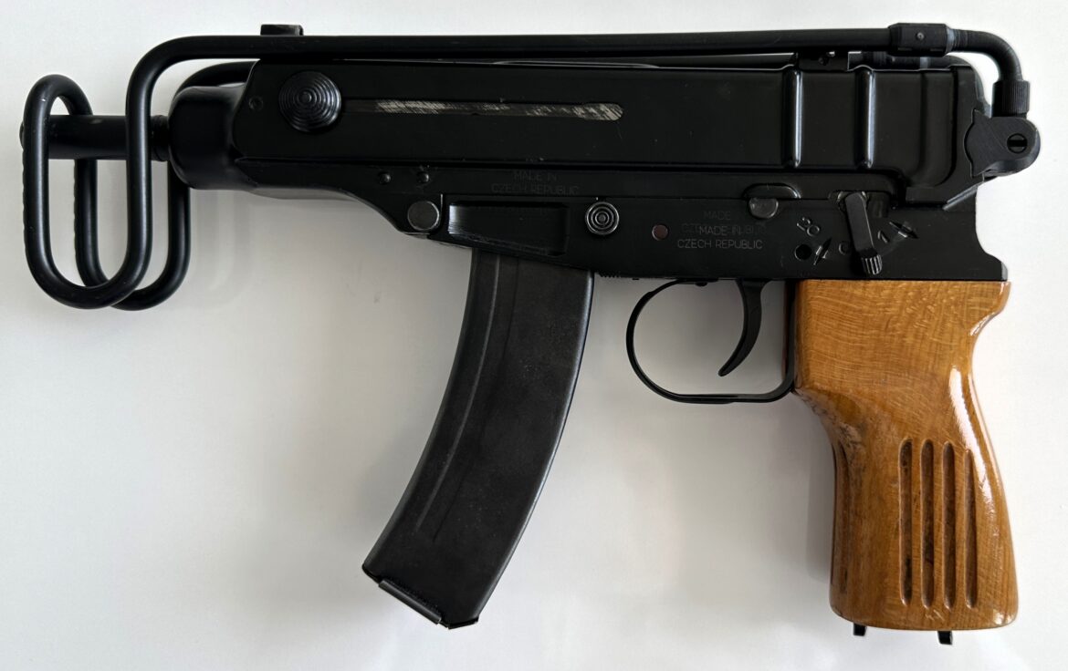 Škorpion s dřevěnou rukojetí, zahnutým zásobníkem a sklopenou ramenní opěrkou.