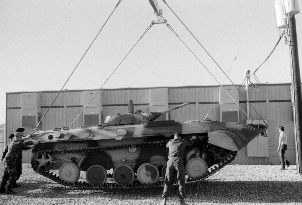 Sovětské bojové vozidlo BMP-1 zvedané jeřábem ve vojenském areálu.