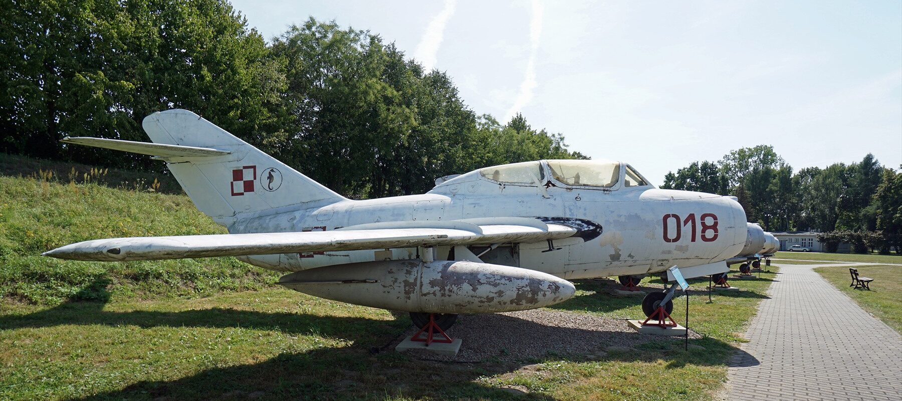 Stříbrný proudový stíhací letoun MiG-15 vystavený na travnaté ploše muzea