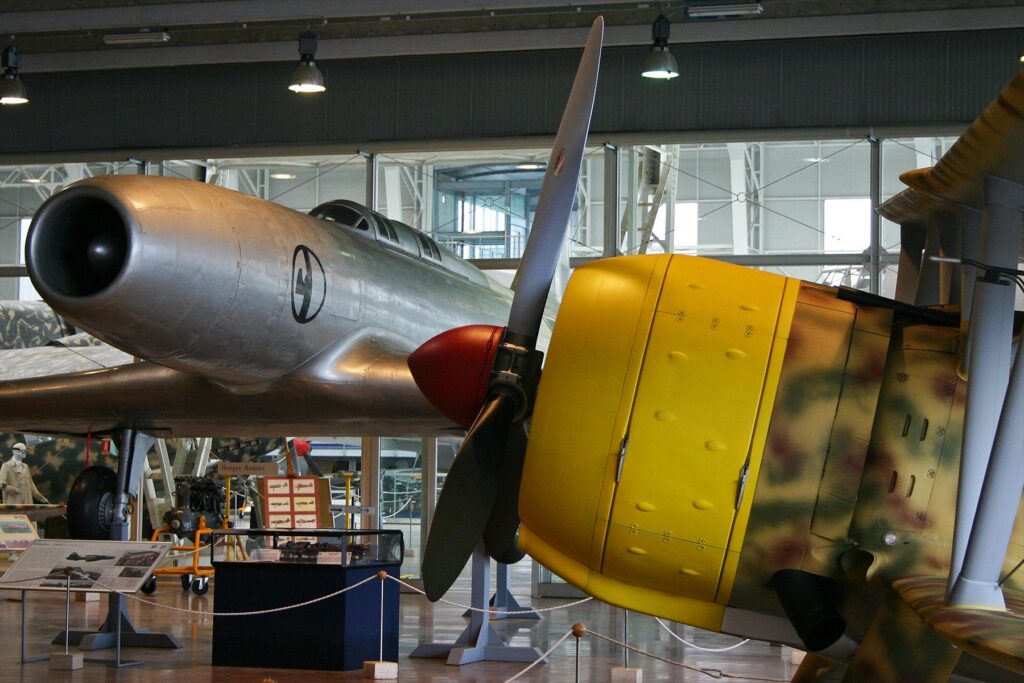 Letoun Caproni Campini N.1 v popředí a italský stíhací dvouplošník Fiat CR.42 v pozadí muzejní expozice.