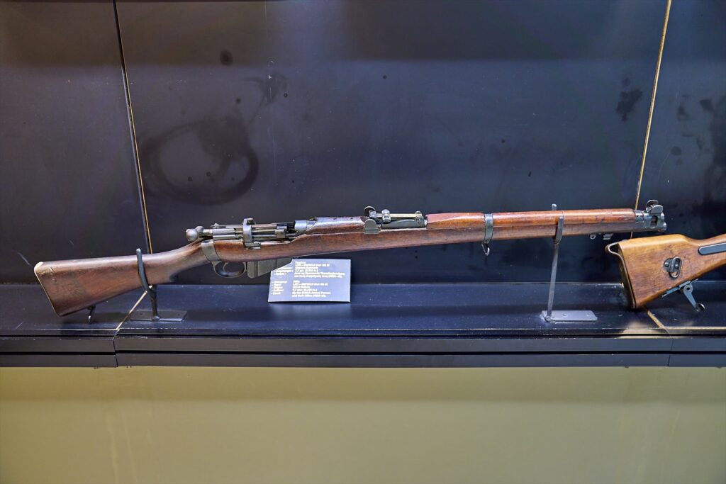 Puška Lee-Enfield No. 1 Mk III s dřevěnou pažbou a předpažbím ve vitríně.