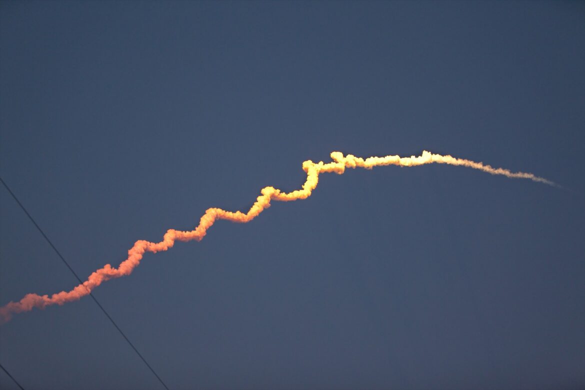 Masivní nosná raketa stoupá k obloze se sloupem plamenů a kouře z odpalovací rampy.