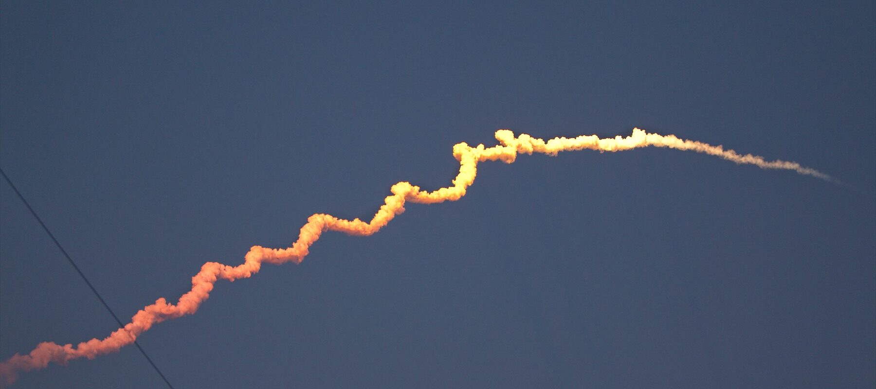 Masivní nosná raketa stoupá k obloze se sloupem plamenů a kouře z odpalovací rampy.