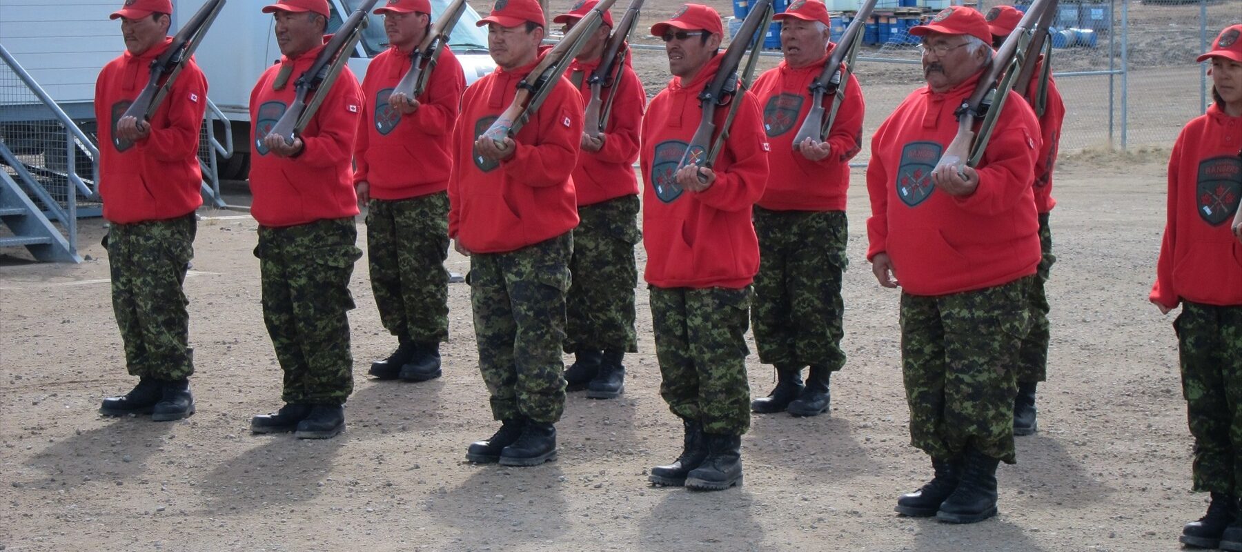 Kanadští Rangers v červených mikinách stojí v řadě s puškami Lee-Enfield.