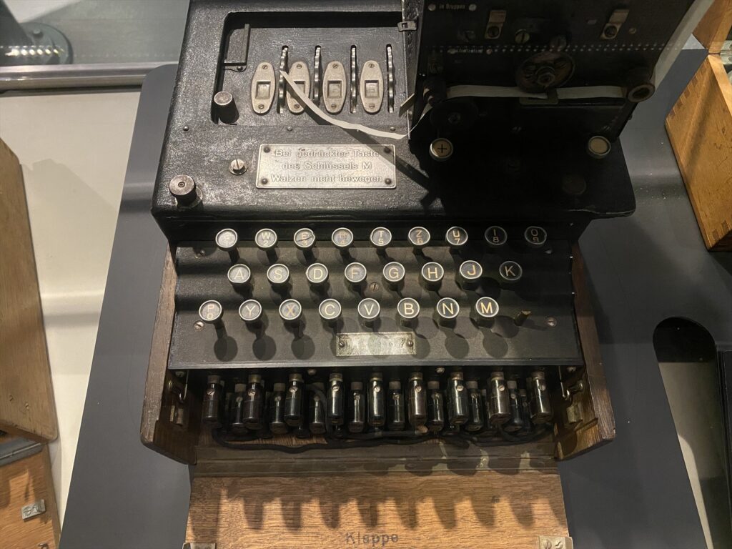Otevřený šifrovací stroj Enigma M4 s klávesami a tiskárnou za sklem muzejní expozice.
