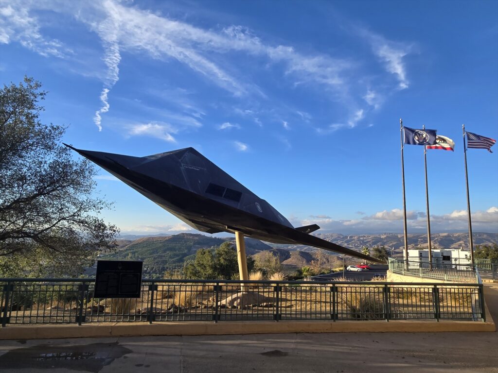 F-117 na venkovním podstavci u prezidentské knihovny, v pozadí kopce a stožáry s vlajkami.