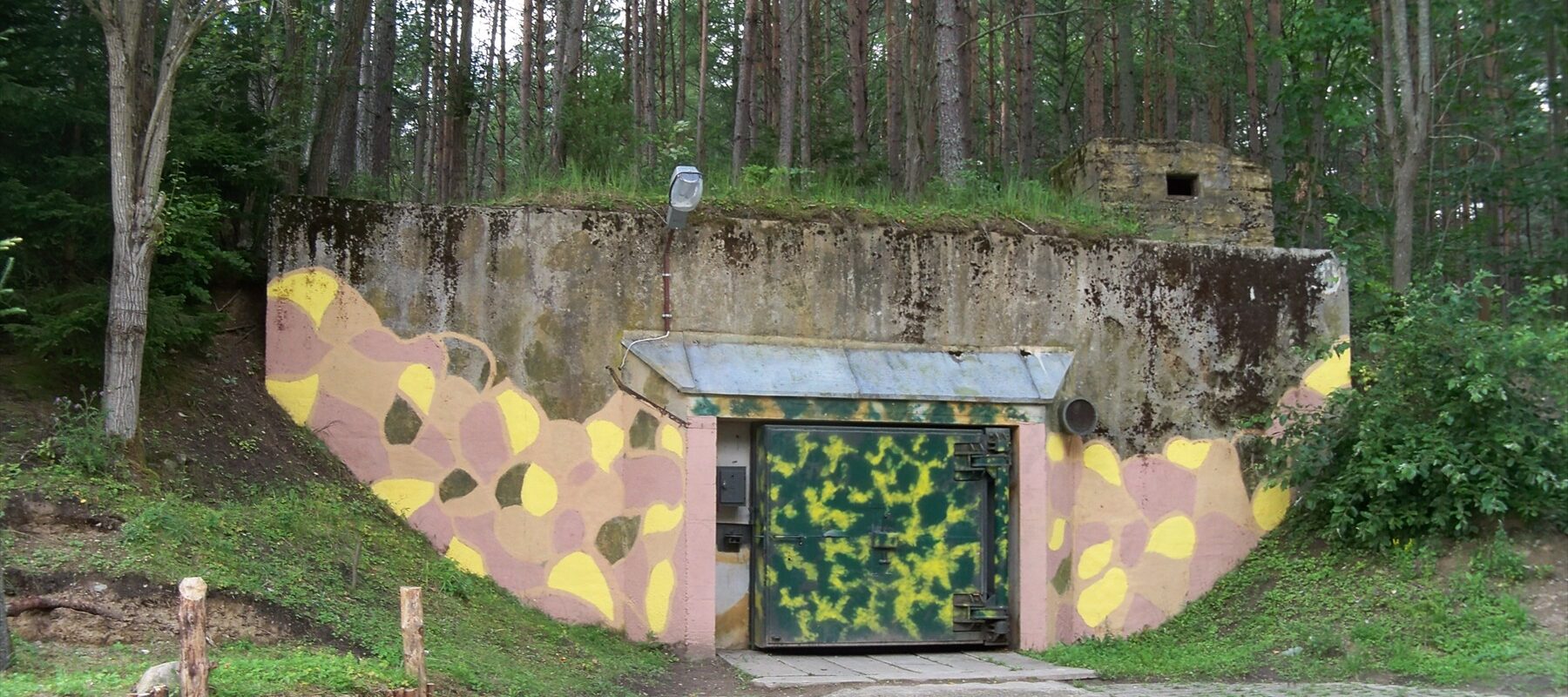 Těžká pancéřová tlaková vrata a betonový vjezd do podzemního vojenského bunkru.