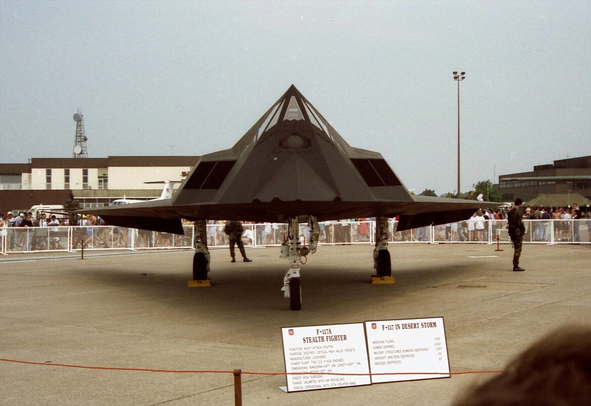 Černý F-117A na podvozku při čelním pohledu, za zábranami stojí návštěvníci.