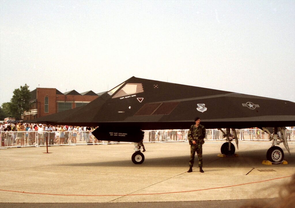 Boční pohled na kabinu a přední část stojícího F-117A, před letounem stojí voják.