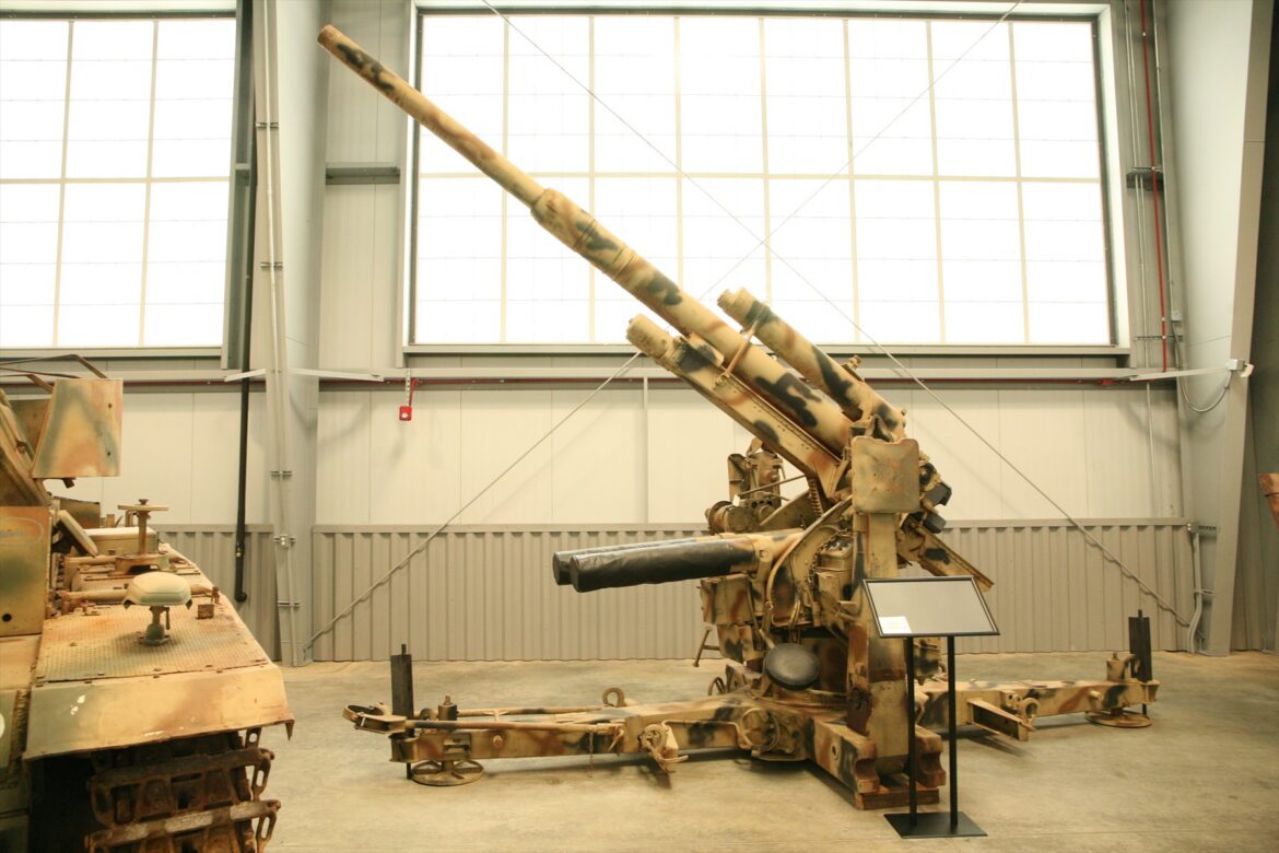 Kamuflovaný protiletadlový kanon Flak 36 na křížové lafetě v muzejní hale.