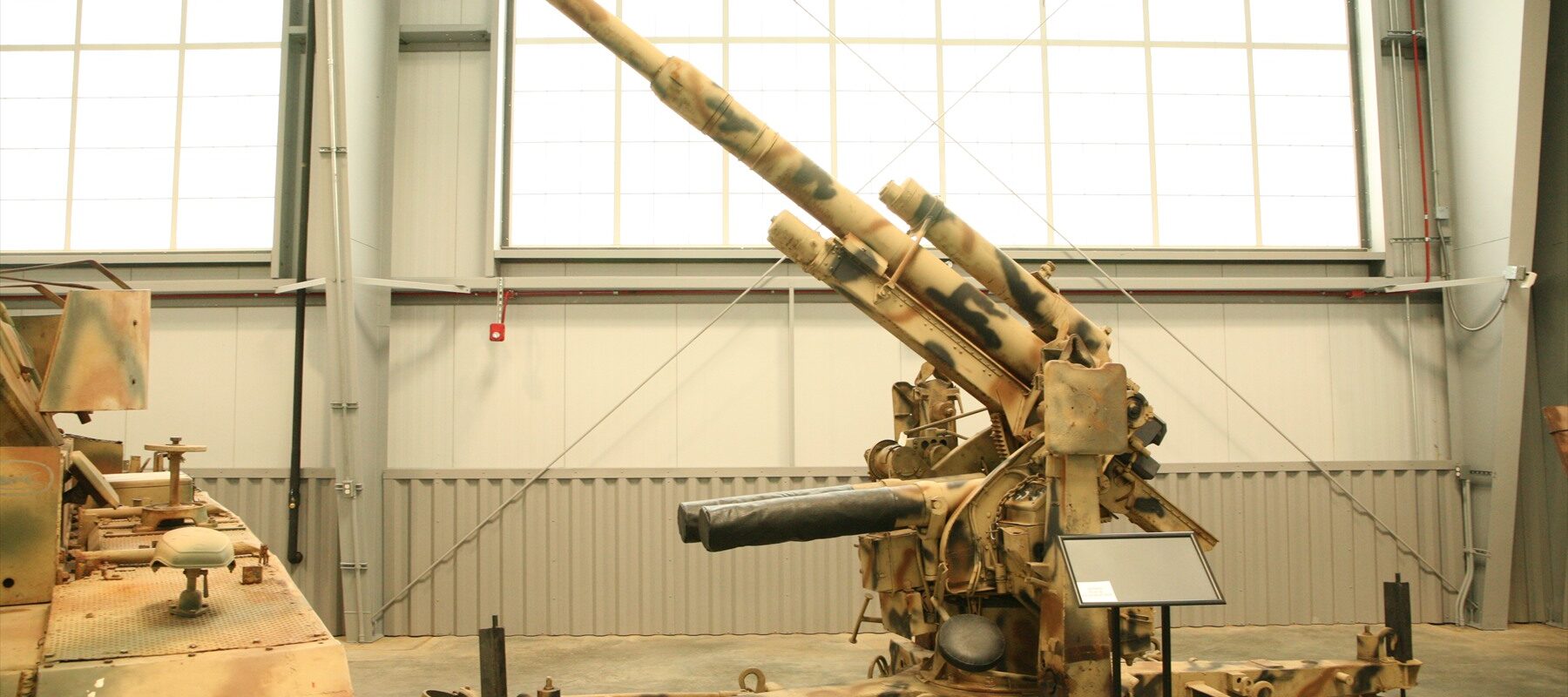 Kamuflovaný protiletadlový kanon Flak 36 na křížové lafetě v muzejní hale.