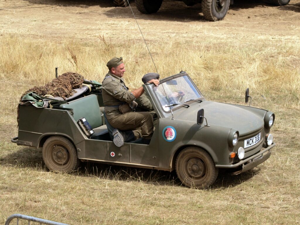 Otevřený zelený Trabant Kübel se dvěma lidmi na přehlídce, pohled šikmo zepředu.