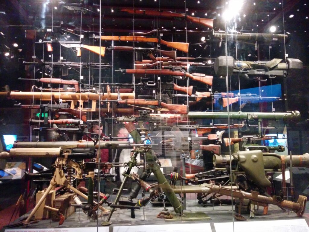 Vitrína s puškami, kulomety a další výzbrojí; v horní střední části je Lee-Enfield s puškohledem.