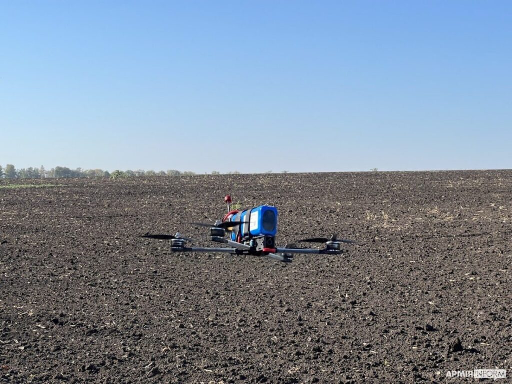 Vojenský kvadrokoptérový FPV dron s připevněnou bojovou hlavicí položený na zemi.