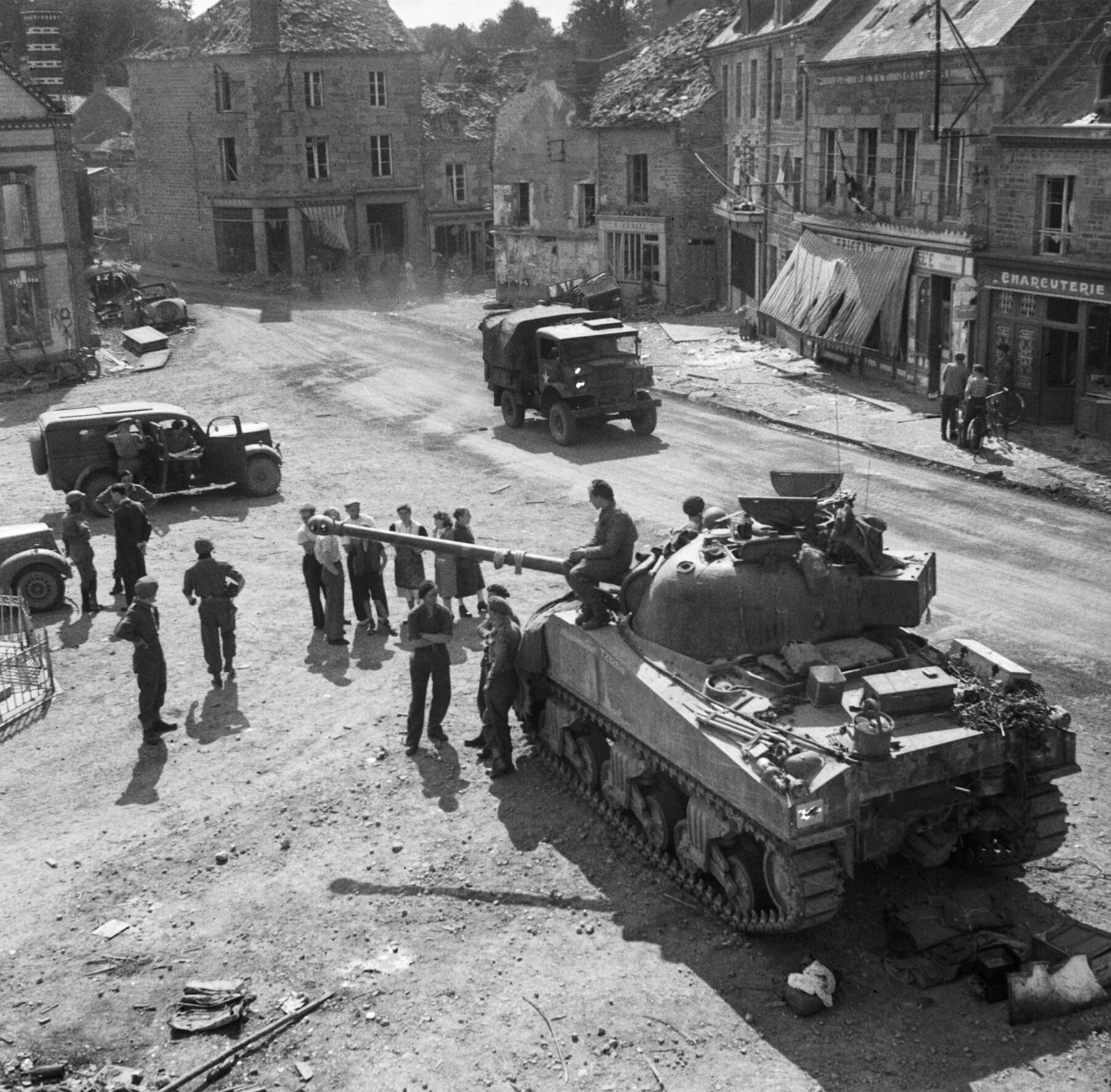 Britský tank Sherman Firefly s maskovací kamufláží projíždí ulicí francouzského města během bojů v Normandii