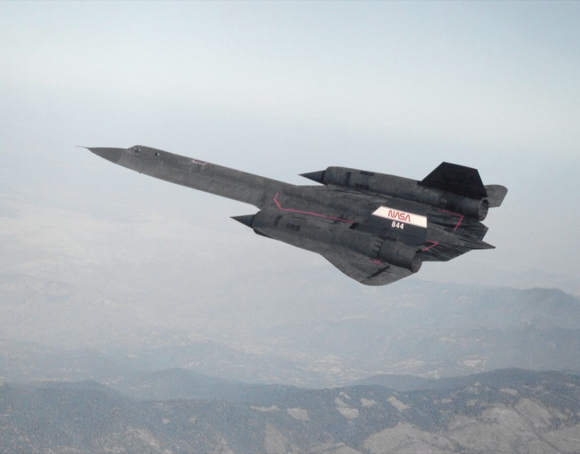 Průzkumný letoun Lockheed SR-71 Blackbird v letu nad horami, pohled shora s dlouhými trupovými přechody a delta křídlem