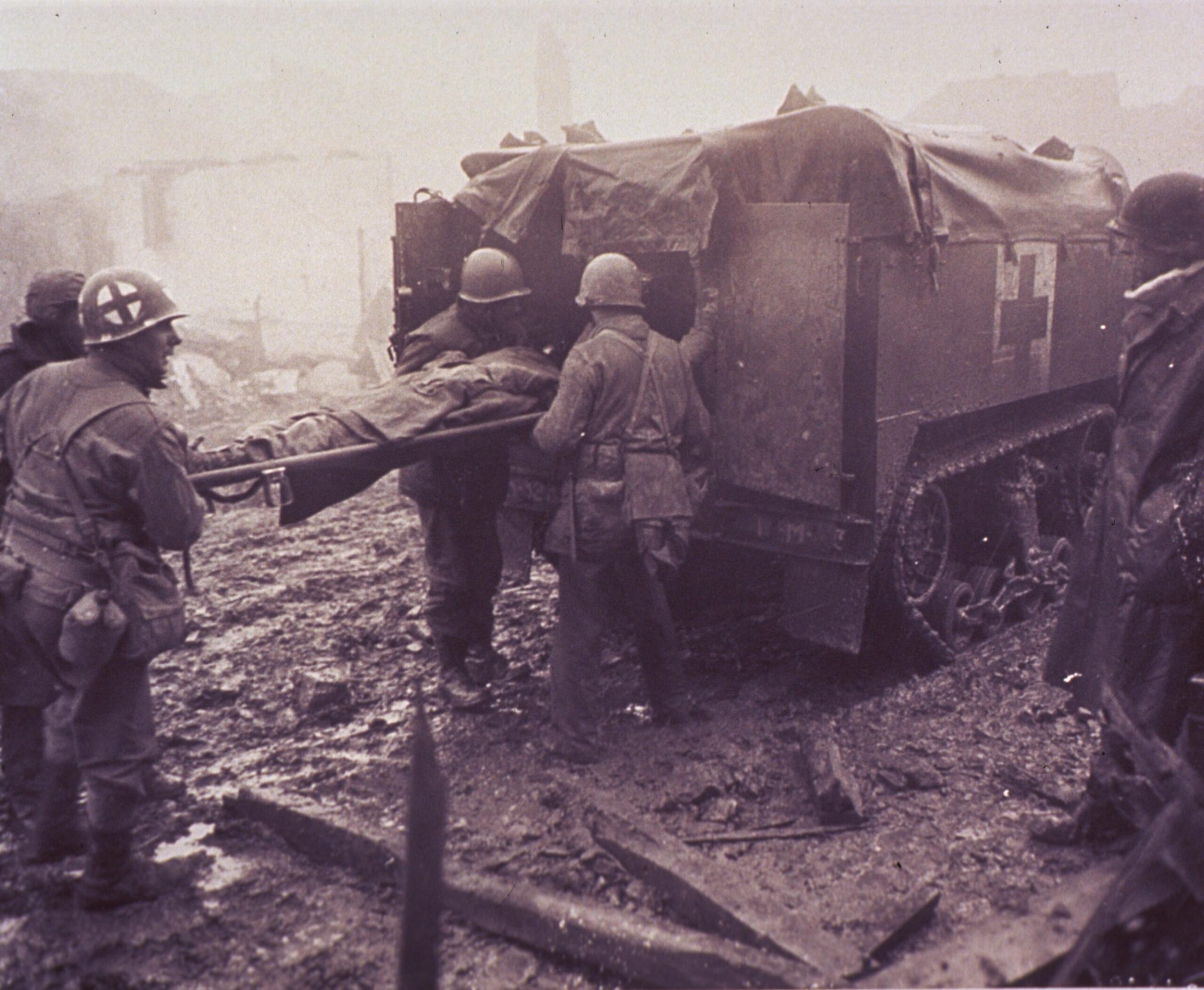 Američtí vojáci nakládají raněného spolubojovníka do otevřeného polopásového transportéru M3 Half-track