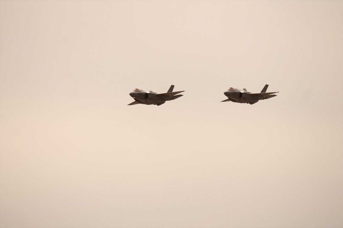 Dva americké F-35A letí ve formaci proti světlé obloze.