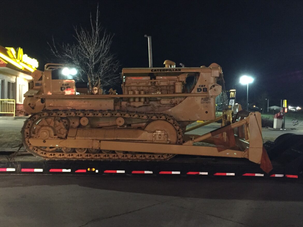 Těžký civilní pásový traktor Caterpillar D8 stojící na trávě s viditelným podvozkem a mohutnými pásy.