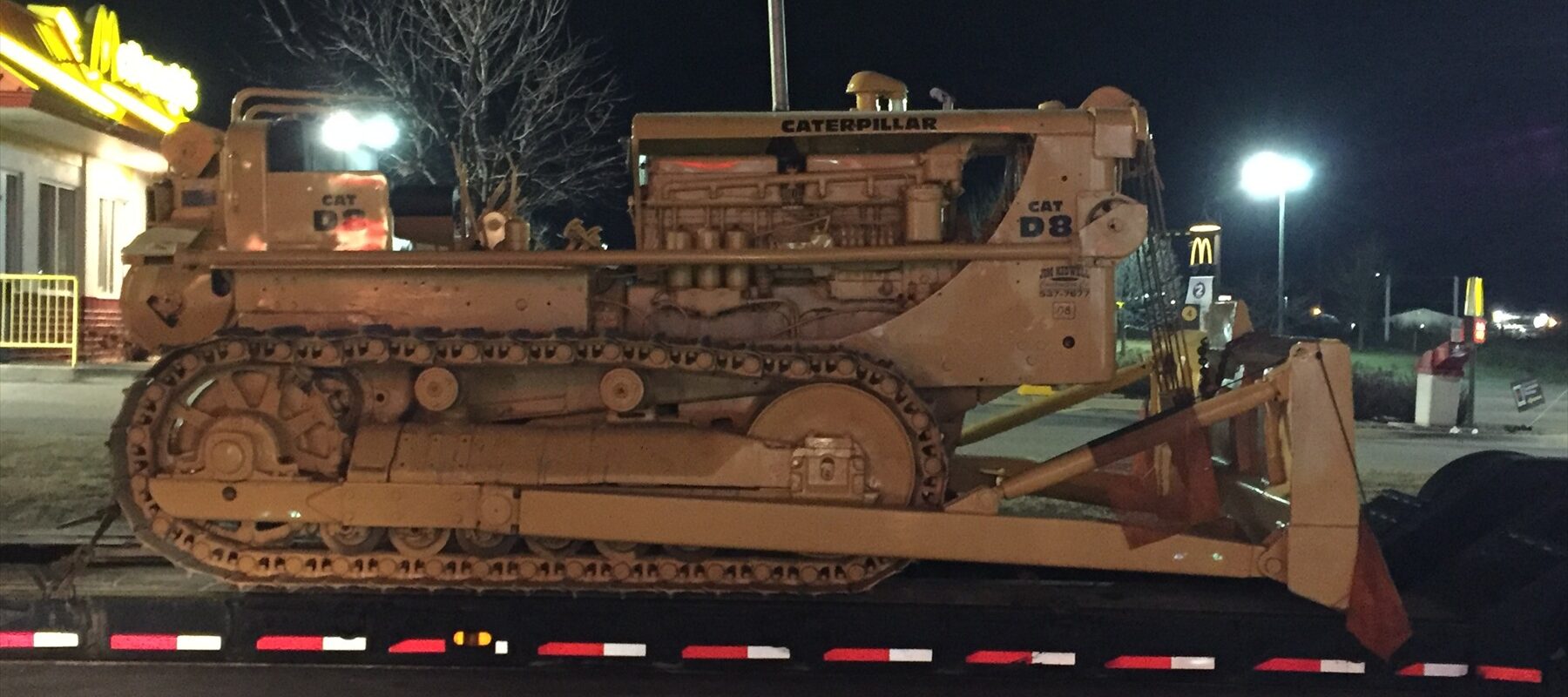Těžký civilní pásový traktor Caterpillar D8 stojící na trávě s viditelným podvozkem a mohutnými pásy.