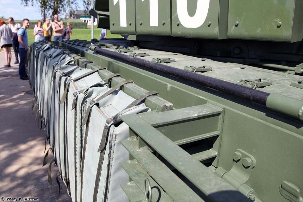 Detail boku T-72B3 s přídavnými ochrannými prvky nad pásy na statické výstavě.
