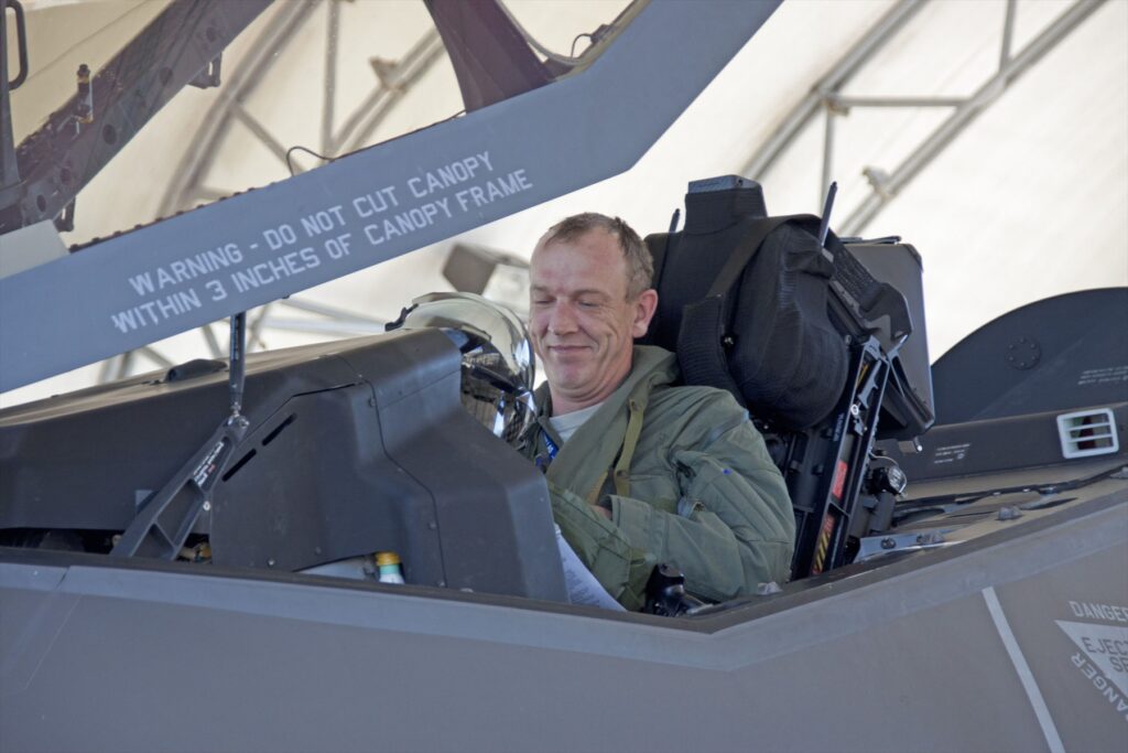Vojenský pilot s přilbou vybavenou průhledovým displejem sedící v pilotní kabině stíhacího letounu F-35.