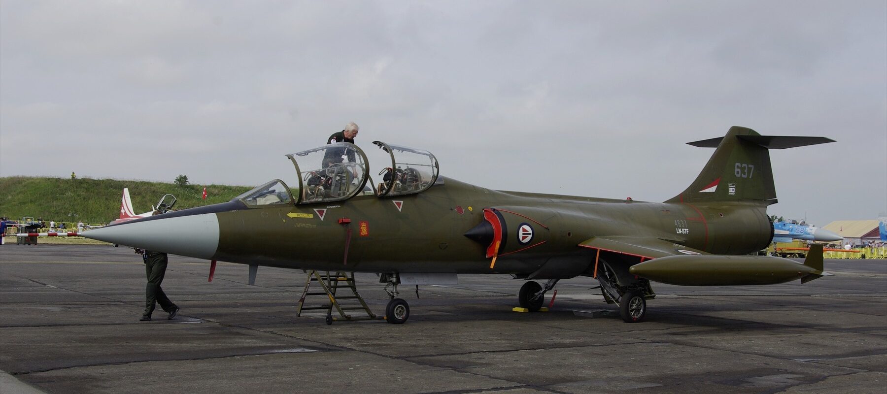 Zelený dvoumístný Starfighter LN-STF s číslem 637 a otevřenými kabinami na letištní ploše.