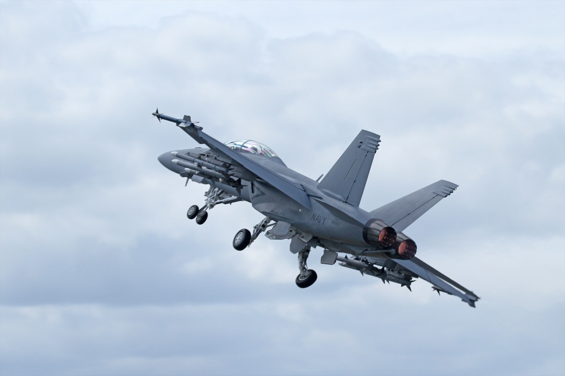 Americký Super Hornet stoupá s vysunutým podvozkem a výzbrojí pod křídly.