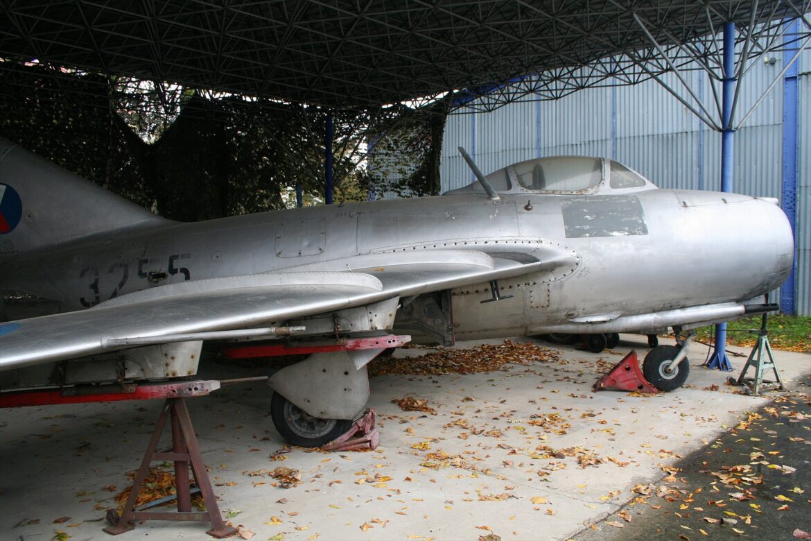 Stříbrný proudový stíhací letoun MiG-15 se šípovým křídlem a československými výsostnými znaky v muzejní expozici
