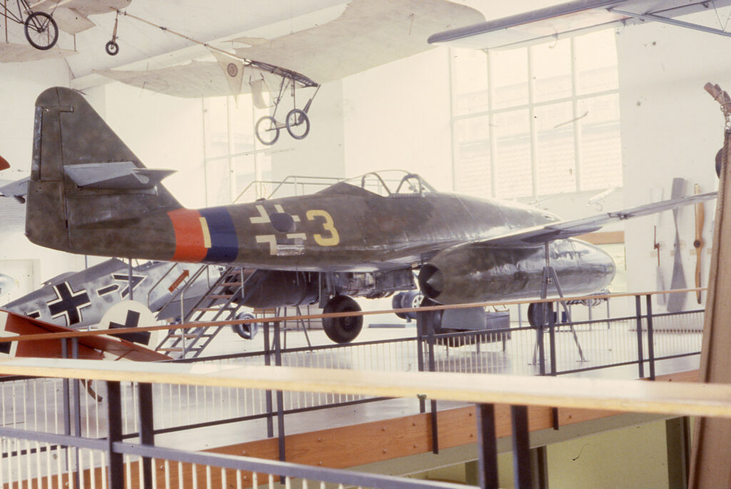 Messerschmitt Me 262 s vysunutým podvozkem na muzejní expozici, fotografovaný z levé zadní strany.