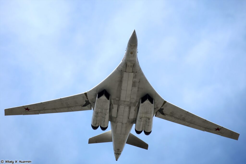 Bílý čtyřmotorový bombardér Tu-160 letící proti modré obloze.