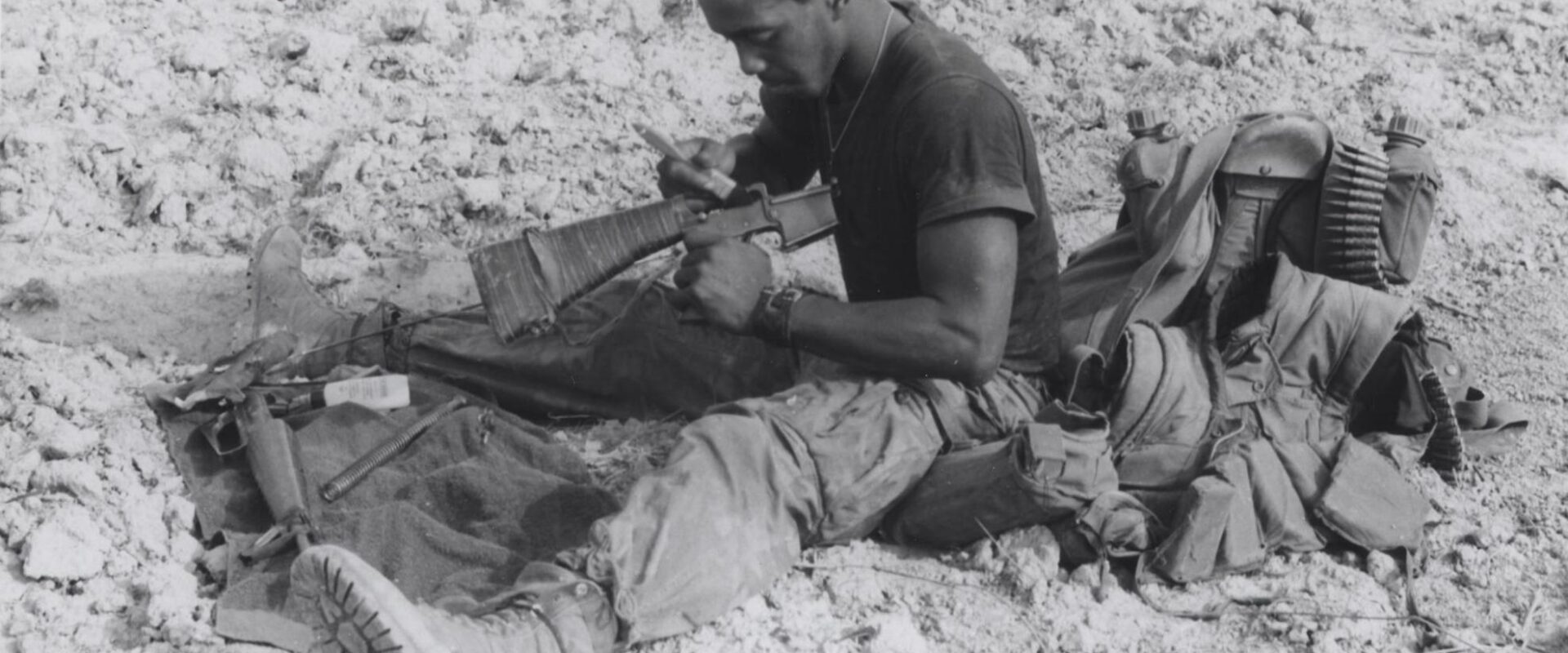 Carl Witherspoon sedí v terénu a čistí rozebranou pušku M16