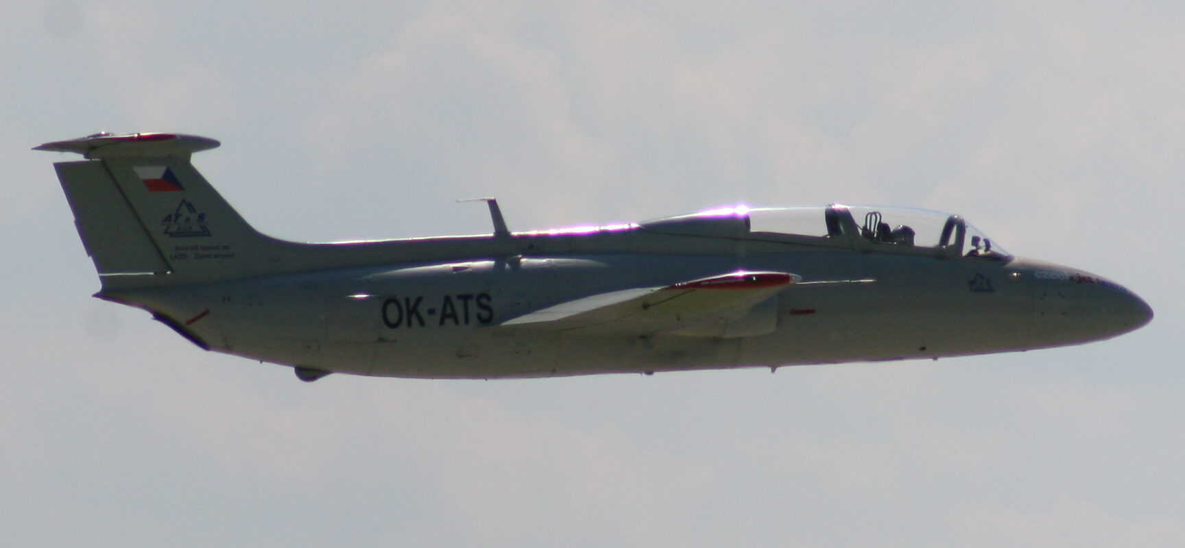Stříbrný dvoumístný L-29 Delfín OK-ATS v letu se zataženým podvozkem.