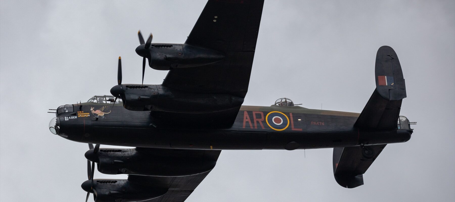 Čtyřmotorový těžký bombardér Avro Lancaster v maskovacím nátěru za letu na letecké přehlídce