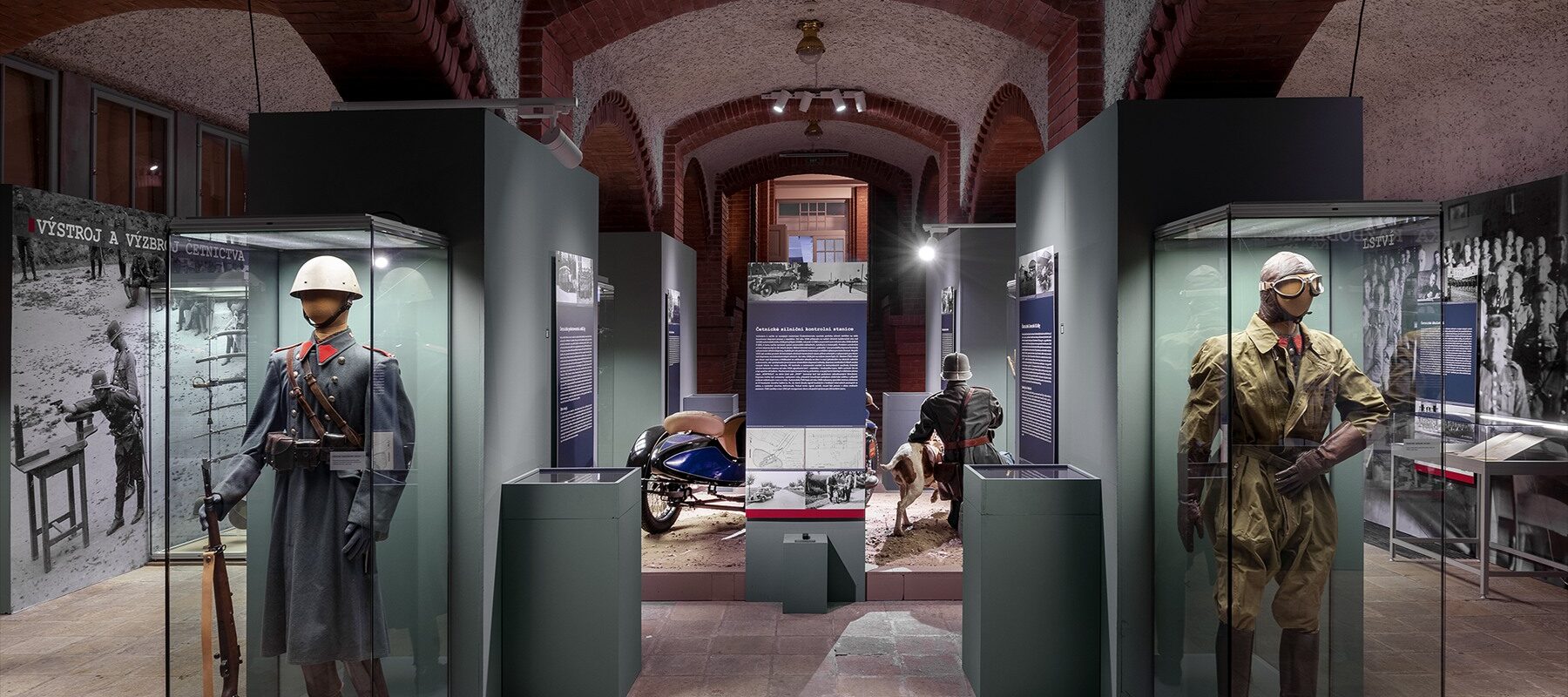 Muzejní expozice dobových stejnokrojů a výstroje četnictva s ocelovou přilbou ve vitríně