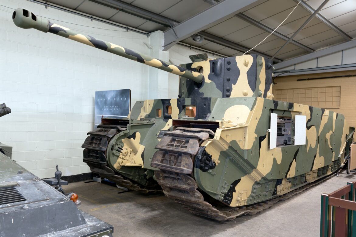 Těžký britský tank TOG II s mohutnou věží, dlouhým kanónem a kamuflážním nátěrem v muzejní hale v Bovingtonu.