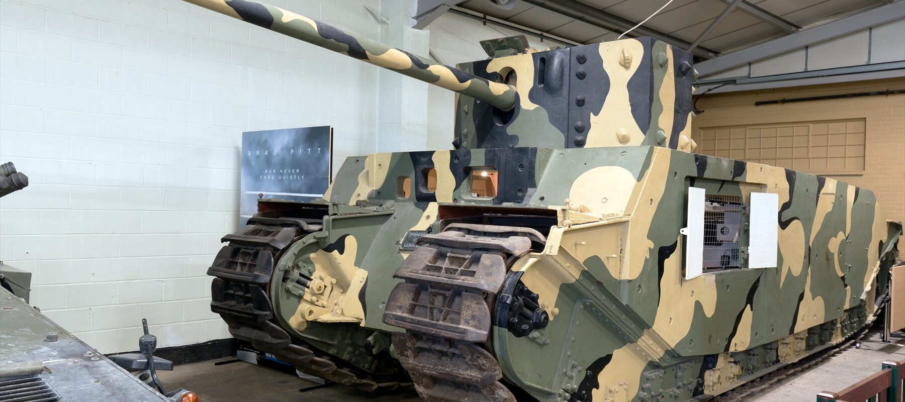 Těžký britský tank TOG II s mohutnou věží, dlouhým kanónem a kamuflážním nátěrem v muzejní hale v Bovingtonu.