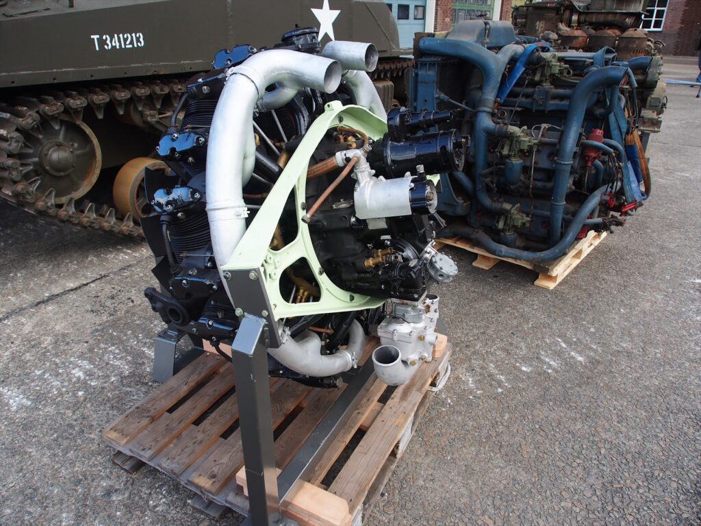 Hvězdicový motor Continental R975 v popředí muzejní expozice, za ním modrý Chrysler A57.