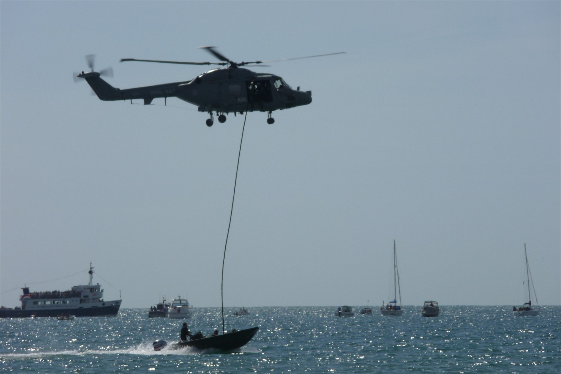 Vrtulník Royal Navy nad mořem se spuštěným lanem k motorovému člunu.