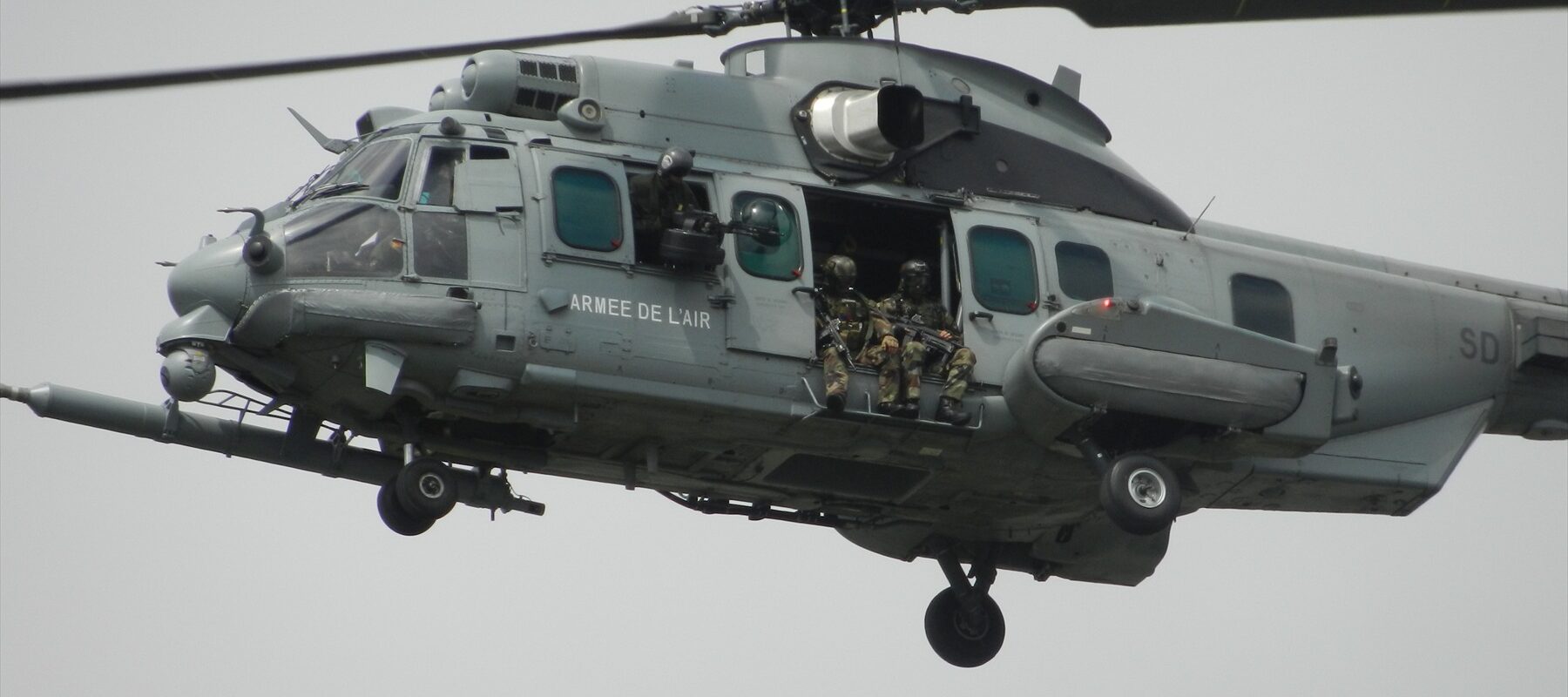 Těžký vojenský vrtulník Airbus EC725 Caracal v šedé kamufláži za letu se sondou pro doplňování paliva