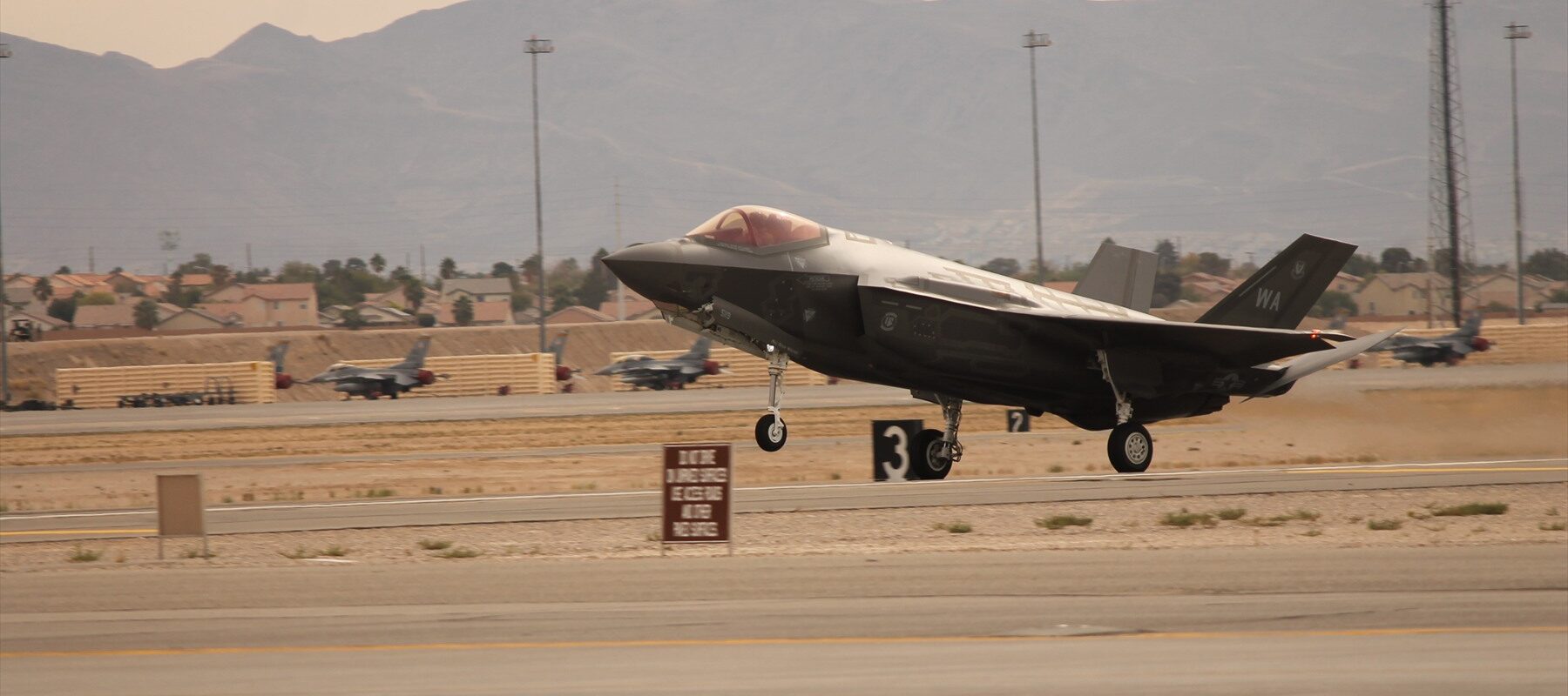 Bojový letoun F-35A Lightning II dosedající na vzletovou a přistávací dráhu se zapnutými pozičními světly a vysunutým podvozkem.