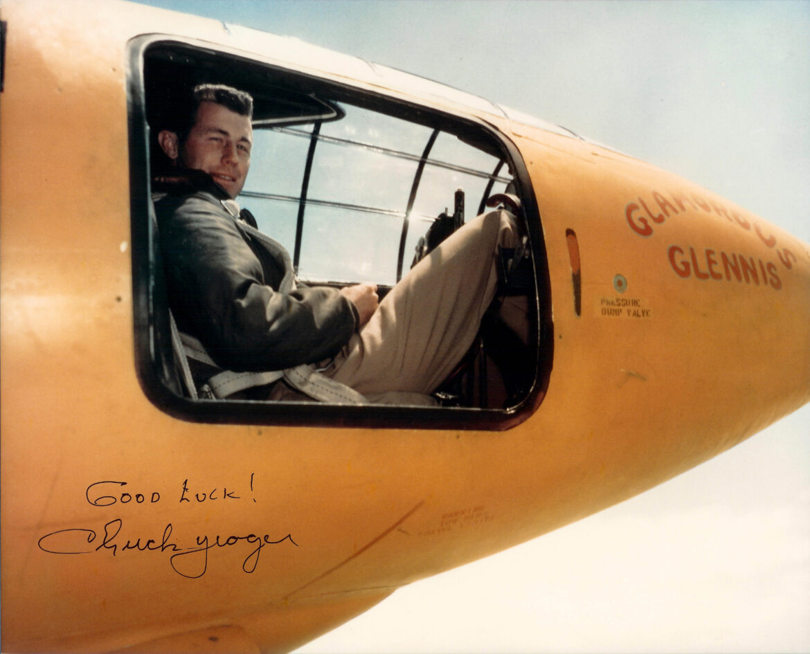 Kapitán Chuck Yeager v pilotní kombinéze stojí u oranžového raketového letounu Bell X1 Glamorous Glennis