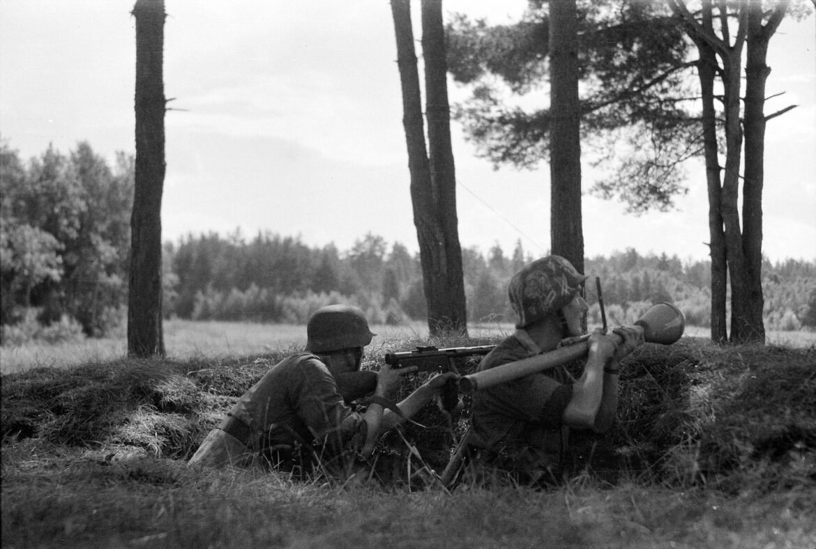 Německý voják v polní uniformě mířící z pancéřové pěsti Panzerfaust s trubicí založenou pod paží.