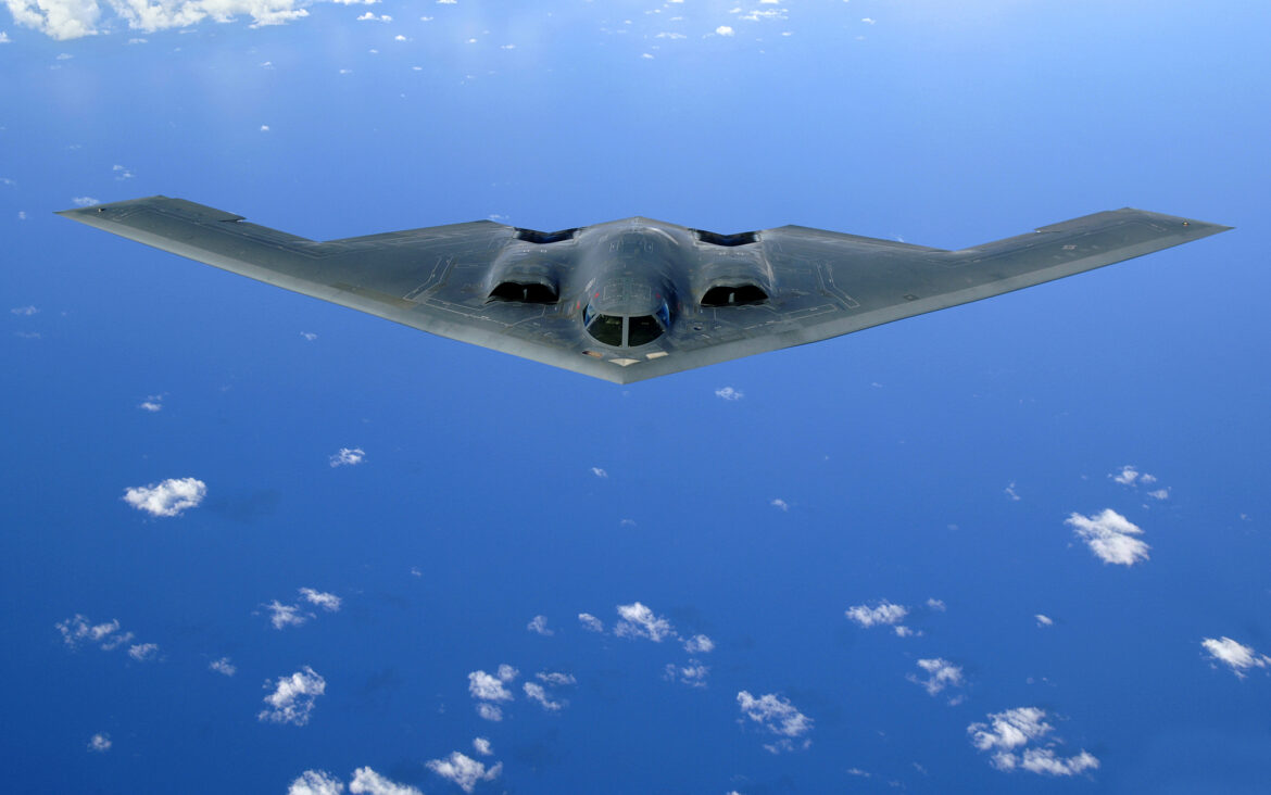 Černý stealth bombardér Northrop Grumman B-2 Spirit bez svislých ocasních ploch letící nad mraky