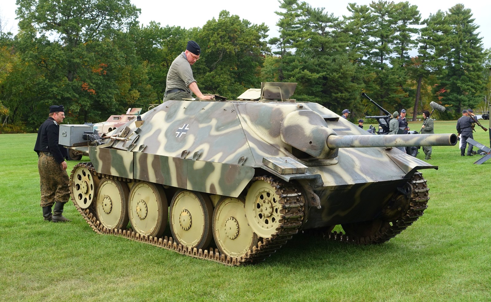 Stíhač tanků Jagdpanzer 38 s nízkou siluetou a maskováním projíždí travnatým terénem během rekonstrukce.
