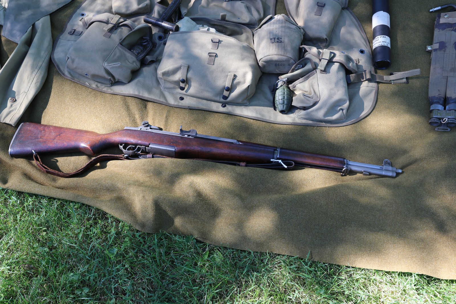 Puška M1 Garand s bodákem, nábojovými pásy a přilbou na vlněné dece.
